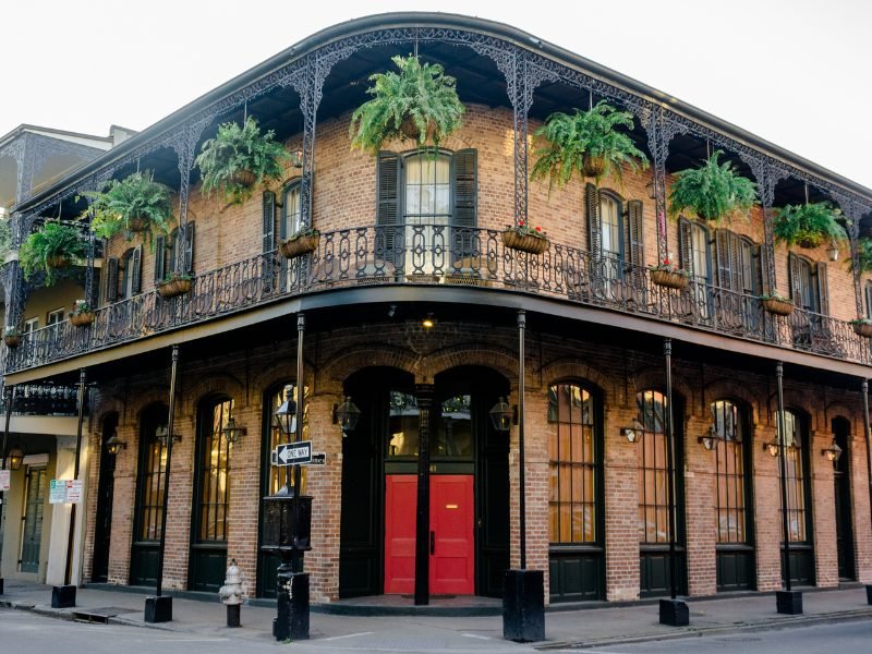 Brick building with rounded porch around the front, ferns in baskets, red door in the French Quarter 