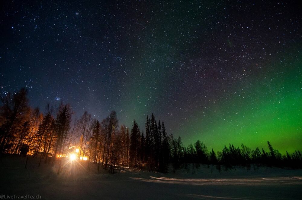 Cabin near Anchorage Alaska with the northern lights on the horizon and a view of a cabin in the distance while watching the northern lgihts