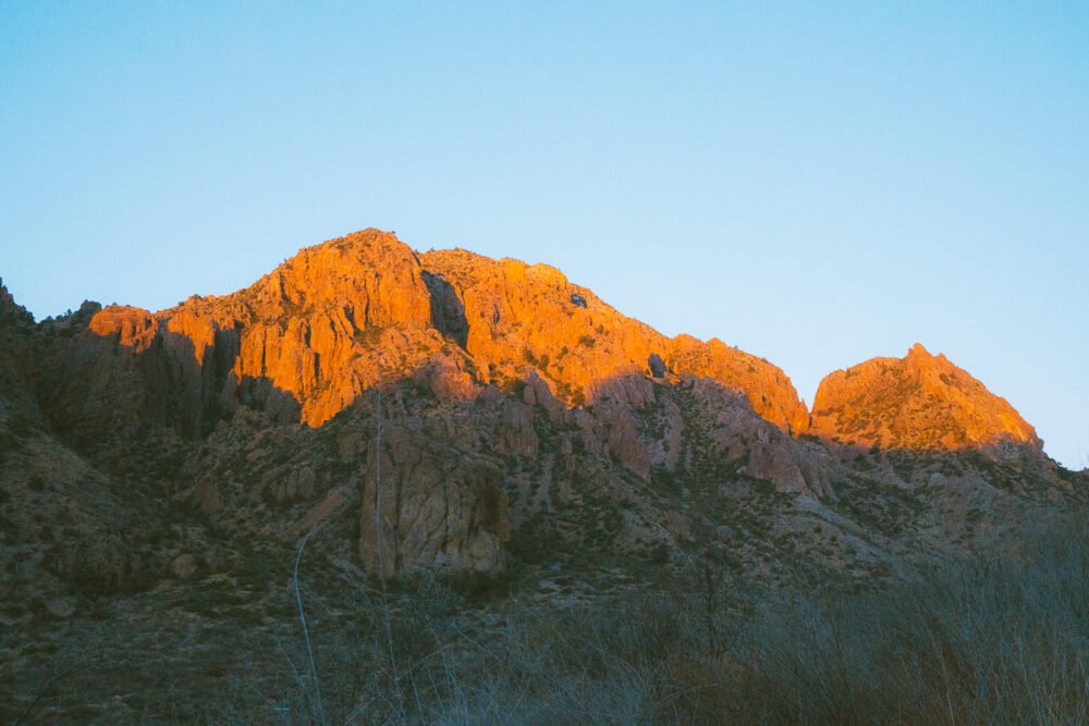 Red rocks in Big Bend National Park in the winter, with shadows forming on the bottom part of the mountains, and sunlight lighting up the tips of the mountains.