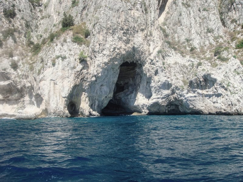 Entrance of the Blue Grotto sea cave in Capri, Italy. The interior of the cave is not visible, just a shadow, but the water around the cave is very blue.