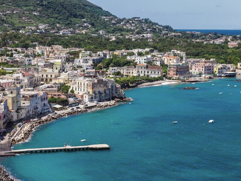 The port of ischia with piers and buildings and beaches on the hillside of a large island