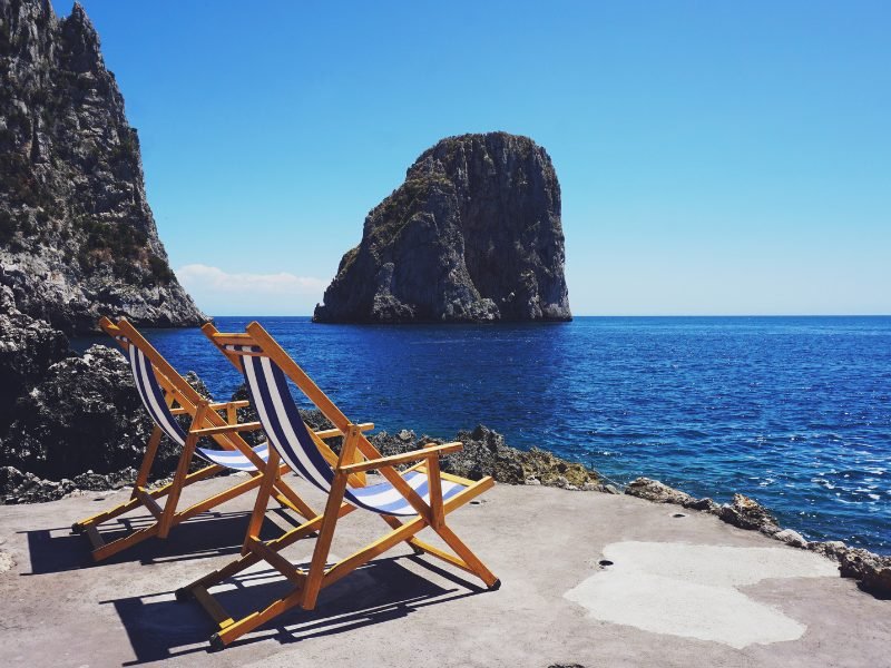 Two beach lounge chairs looking onto the waters of Capri with a small island rock off in the distance.