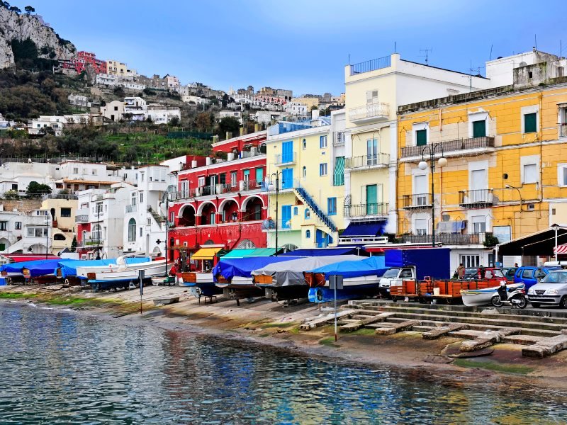 The colorful buildings on the seaside harbor of Capri, buildings in red, yellow and white with boats docked.