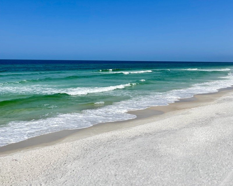 white sand and turquoise water with dark blue water further out at pensacola beach florida