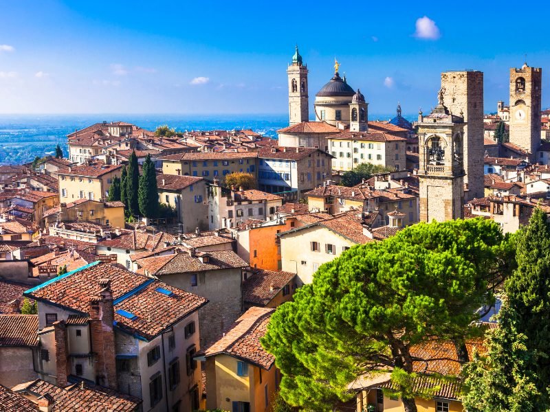 the town of Bergamo italy with towers, churches, and buildings and trees