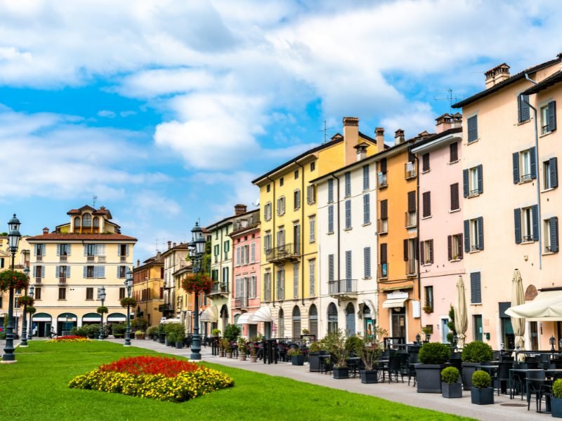 green lawn with yellow and red flowers, with colorful pastel buildings around the grasss, in a plaza in Brescia