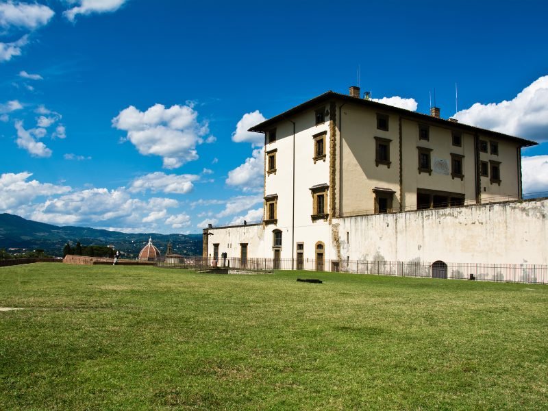 The fortress of Belvedere Forte in Florence, with grass, a fortress fortification, and a view of the Florence skyline behind it.