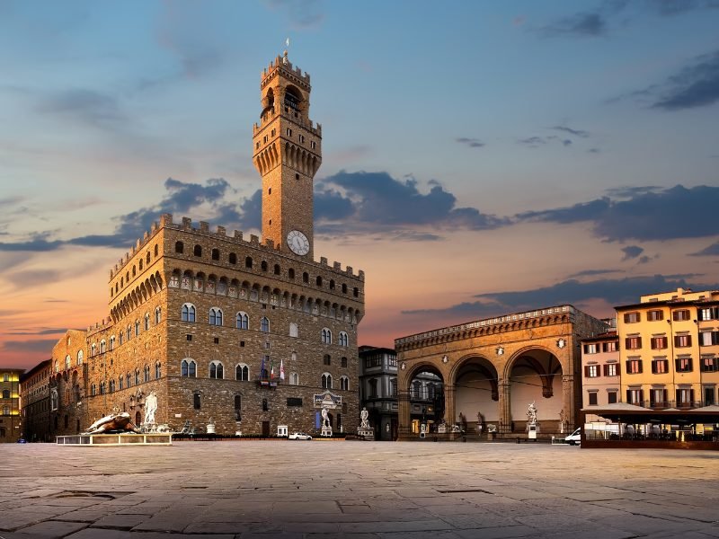 View of a clocktower in a piazza in Florence at sunset with beautiful sky and no people walking about in the middle of the square