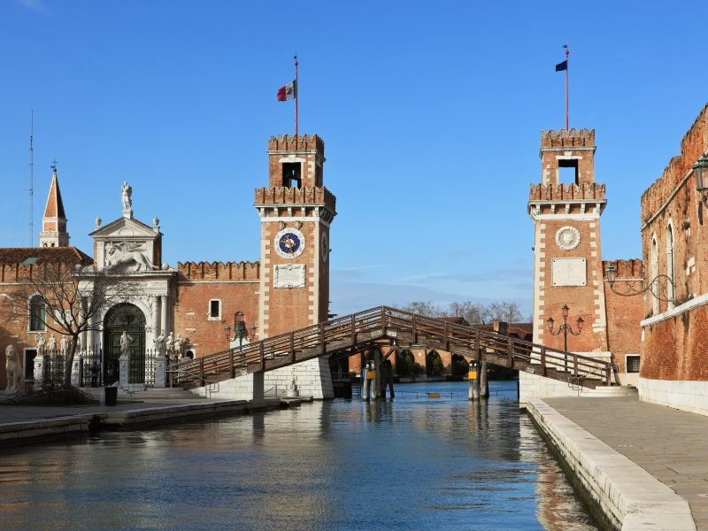 Two towers, connected by a triangular shaped wooden bridge, over a canal