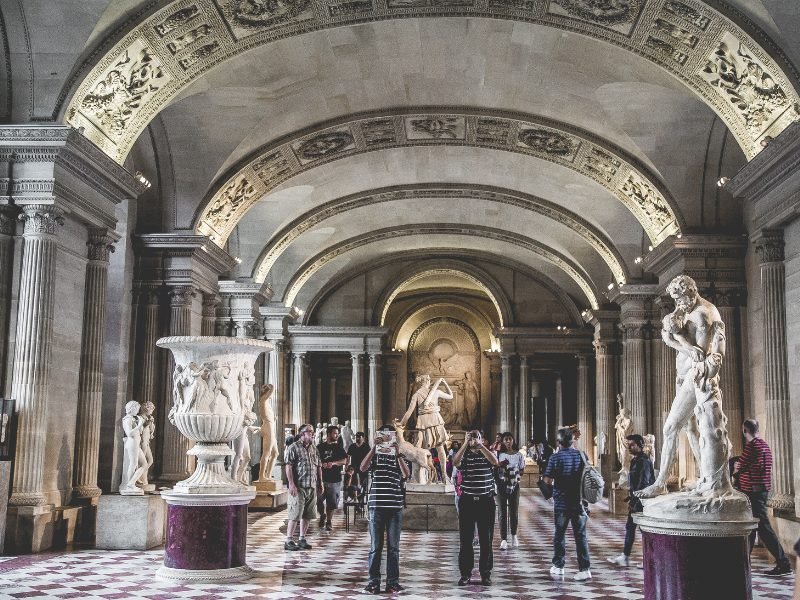 people walking around the interior of the louvre with gray walls and marble details