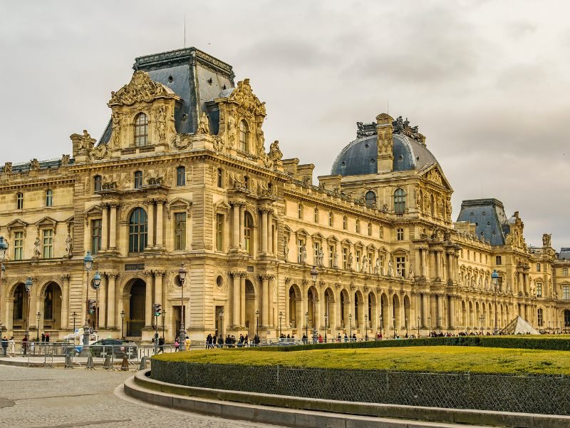 Exterior of the Louvre on a cloudy day, lots of Baroque detailing and fancy style of architecture that shows its roots as a former royal residence for French kings