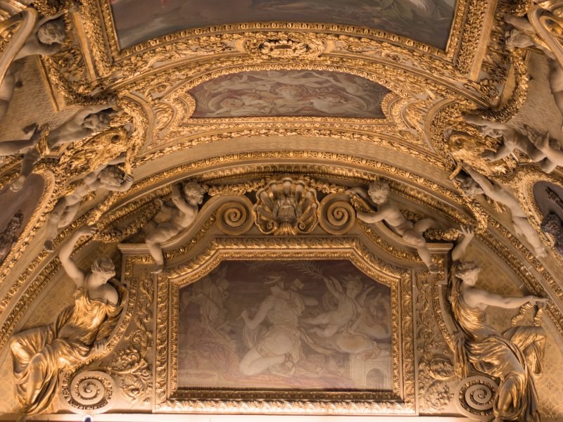 Ornate ceiling work in gold leaf on the ceiling of the Louvre, with angel sculptures and other detailing such as spirals, shells, etc. on the piece