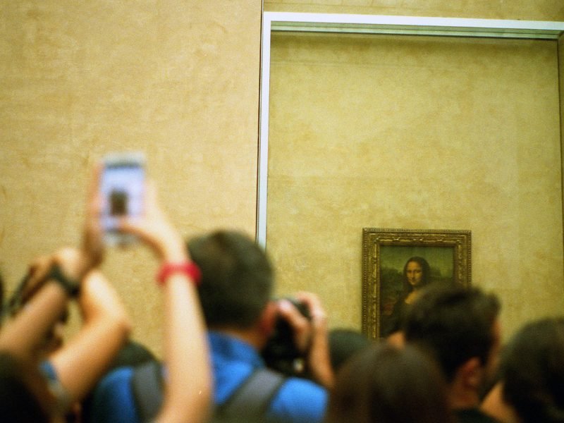 people with cameras trying to get a good angle of the mona lisa in the museum