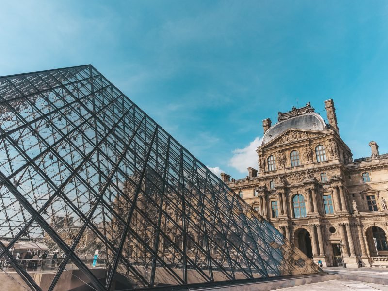 The glass and metal pyramid designed by IM Pei in front of the Baroque front facade of the Louvre, a former royal palace in Paris, on a clear sunny day.