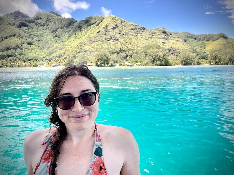 Allison in front of brilliant blue waters and green hilly landscape