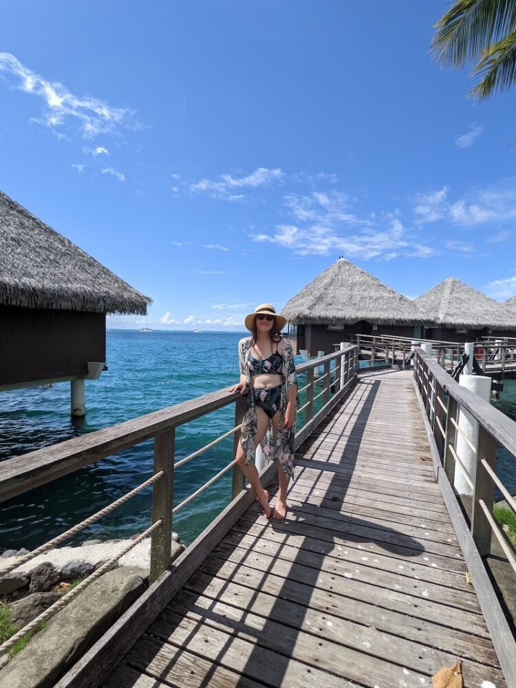 Allison wearing a monstera print swim cover up and a bikini in front of bungalows