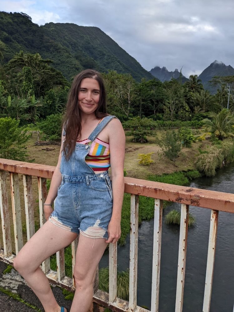 Allison wearing a rainbow shirt and overalls with background of mountains and foggy misty sky