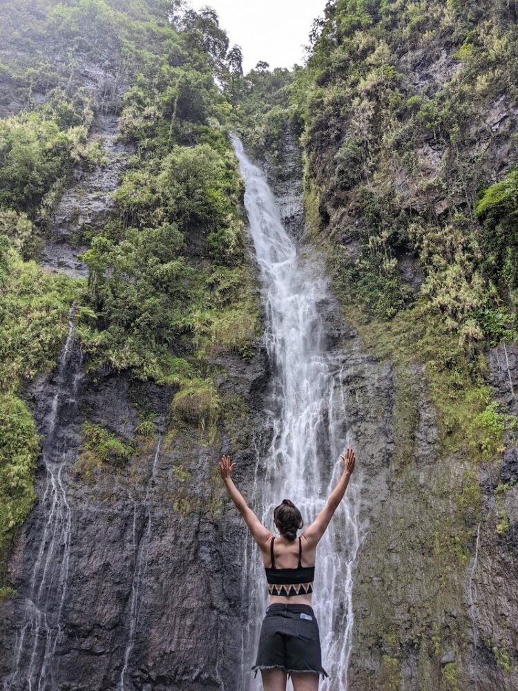 Allison with her back to the camera with her arms in front of a waterfall in Tahiti