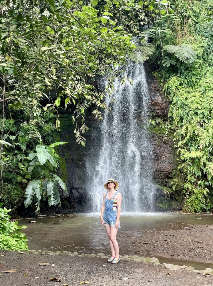 Allison in a rainbow shirt and overalls in front of a waterfall in Tahiti