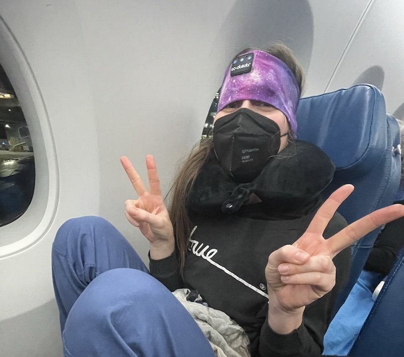 Allison giving two peace signs, wearing a mask, a headband, a mask, a T-shirt that says 'true" and blue pants
