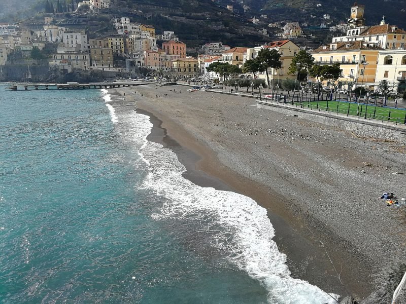 The beach at Spiaggia di Minori with no people on it, perhaps early in the morning or in the off season, a sports field and the town of Minori in the background.