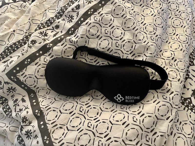 A black sleep mask that says bedtime bliss on it on a bed duvet cover