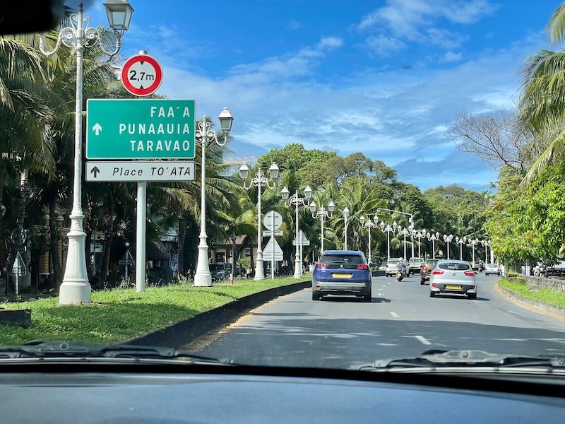 Two-lane road in Tahiti with green street sign leading to Faa'a and other places in Tahiti, with white streetlamps