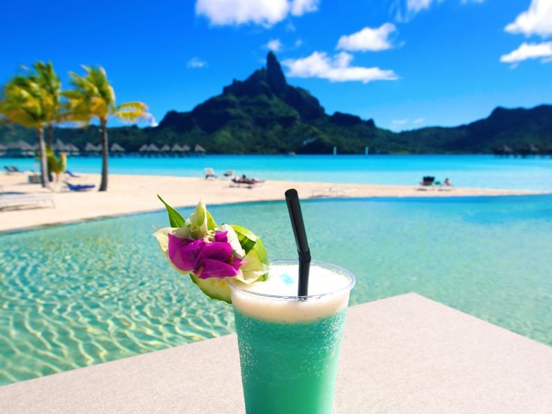 Tropical blue cocktail with pool and overwater bungalows in the background