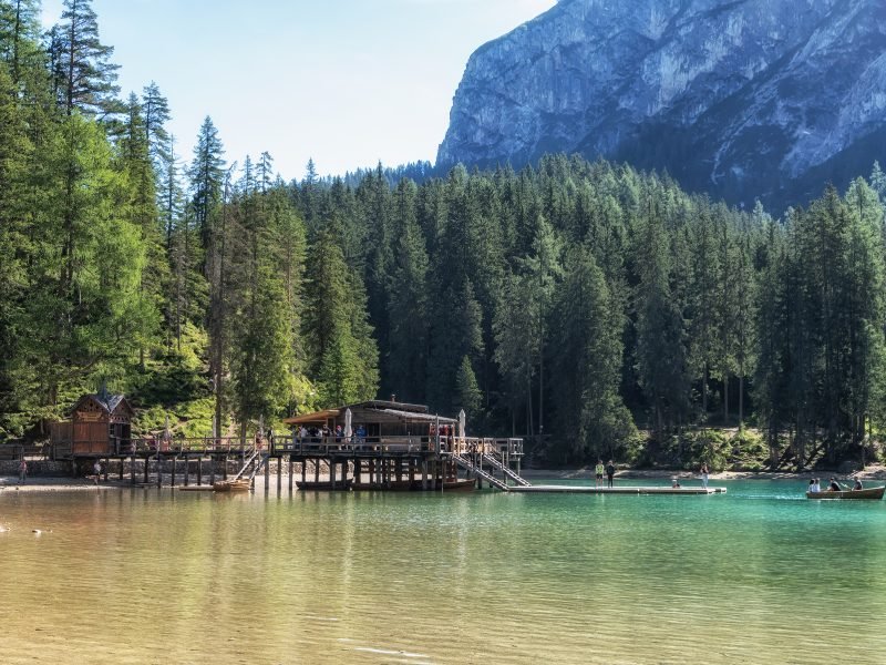 Lago di Braies view of the boathouse from an alternative angle with forest in the background, people in a canoe in the lake