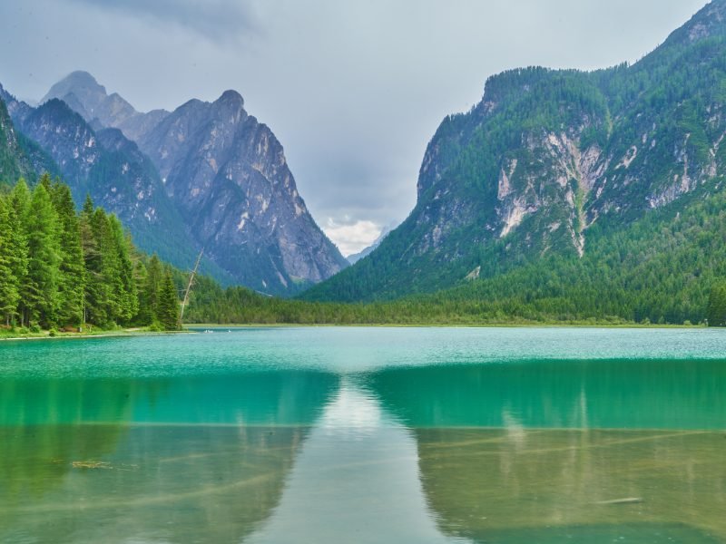 Turquoise lake water, still on a cloudy day, wtih Dolomite mountains in the background