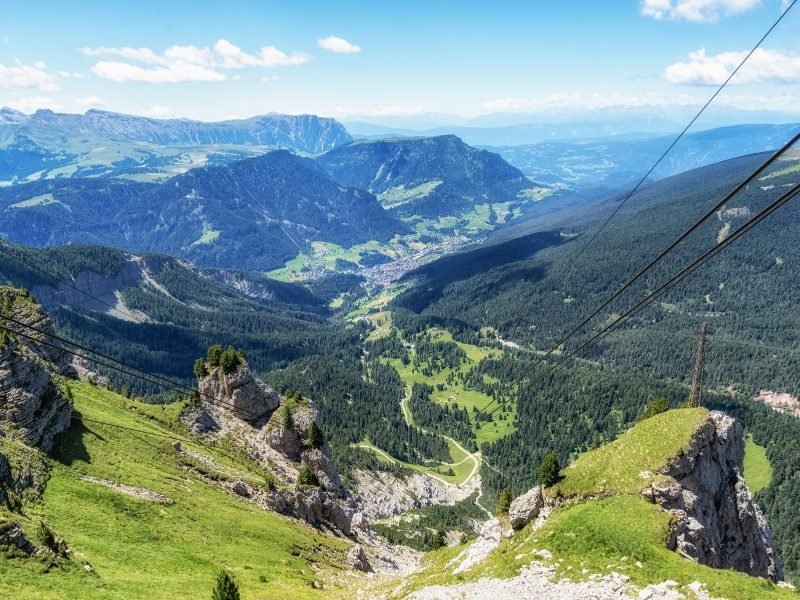 The Seceda cable car up in the mountains, looking down below into the valley below, beautiful view of the Dolomites in green color with trees all aorund it.