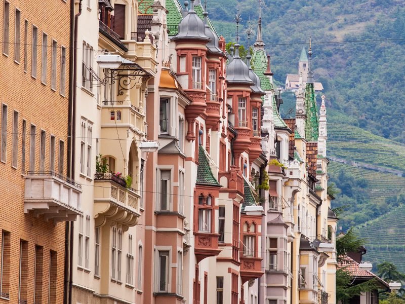 Medieval facades of the buildings in Bolzano with the background of the terraced vineyards and other parts of the mountains of the Dolomites behind the city center.