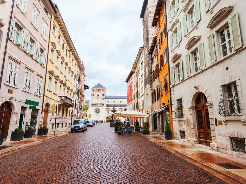 Trento buildings and plaza, floor wet from rain, a few buildings in the historic center, a few cars parked on the road