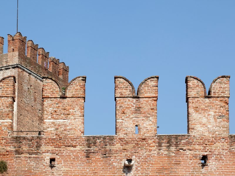 Three turrets along the brick fortress of Castelvecchio against a clear blue sky in Verona, italy