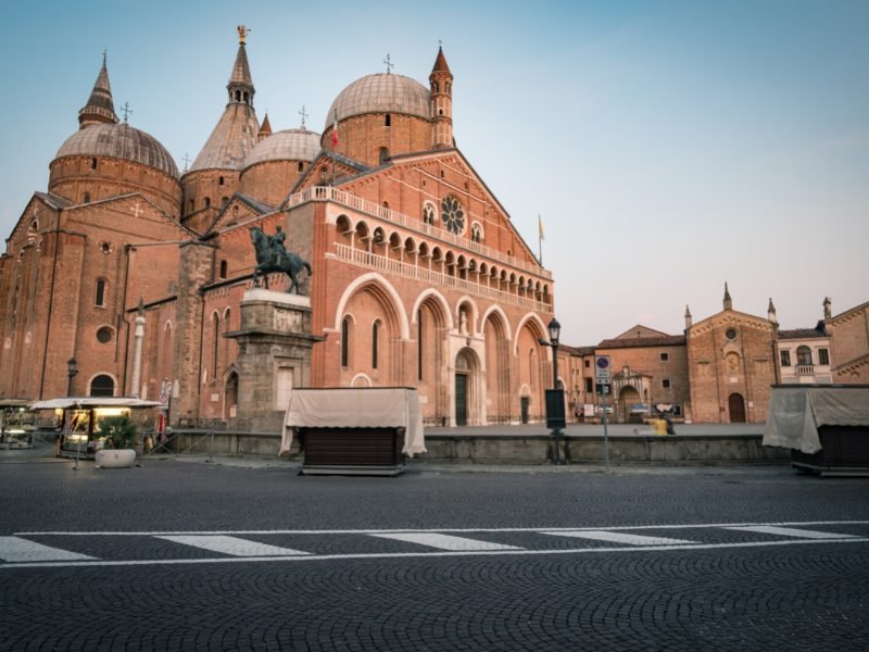 The giant basilica of Padua, in stone work with rounded domes and multiple towers and steeples, and other buildings in the blue hour light