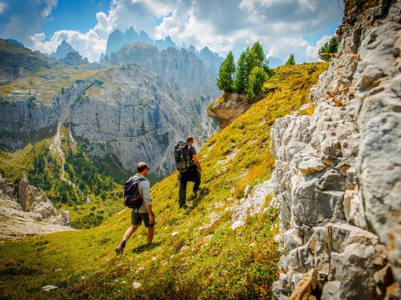 Two men hiking in the Dolomites, wearing backpacks and proper hiking boots, on a sunny day in the Dolomite region of Italy