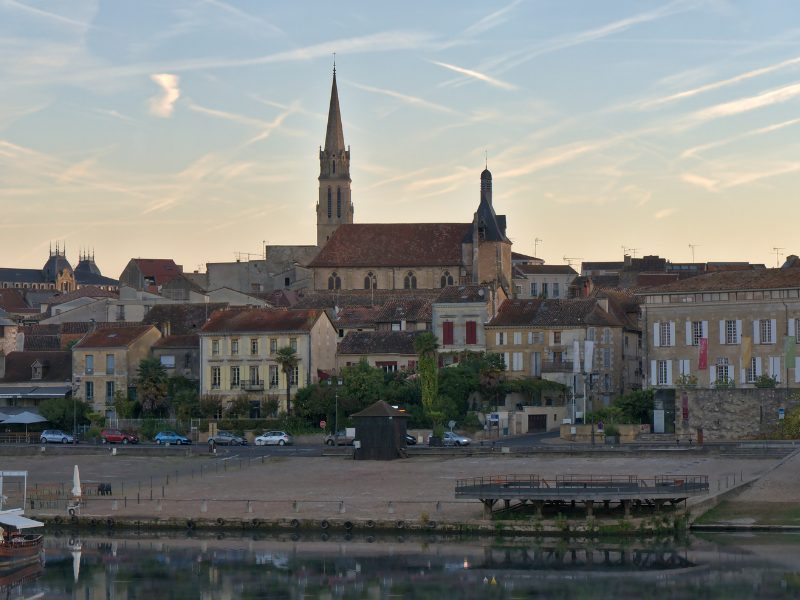 Skyline of Bergerac as seen from across the river, with a church standing tall on the city skyline, around sunset time with streaky clouds
