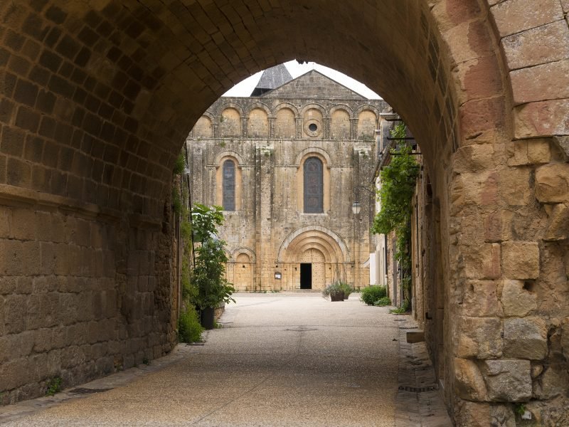 Peeking through a stone archway to admire the abbey of Cadouin, a red limestone style building that is very old
