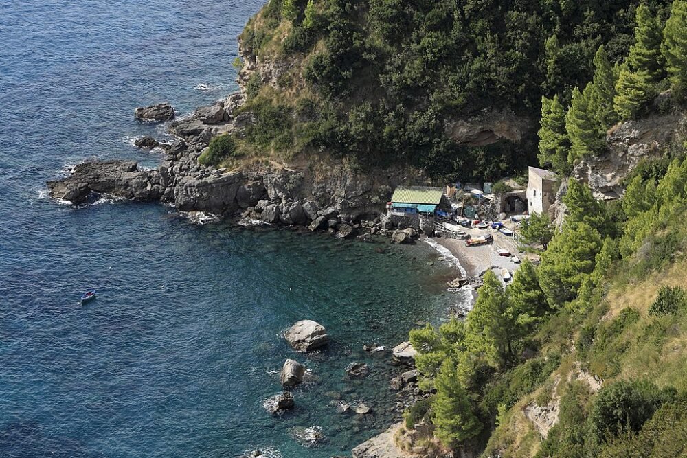 A view from above of a small beach in Italy on the Amalfi Coast with very few people visible on the beach, very deserted and quiet with deep blue sea and rocks