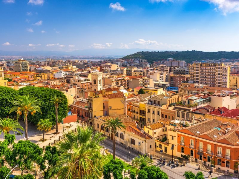 The seaside city of Cagliari, the capital of Sardinia and the start of this road trip. Buildings and palm trees leading out to the sea.