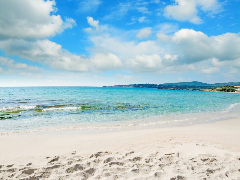 the white sandy beach of le bombarde in sardinia with clear waters and slightly cloudy sky, empty beach