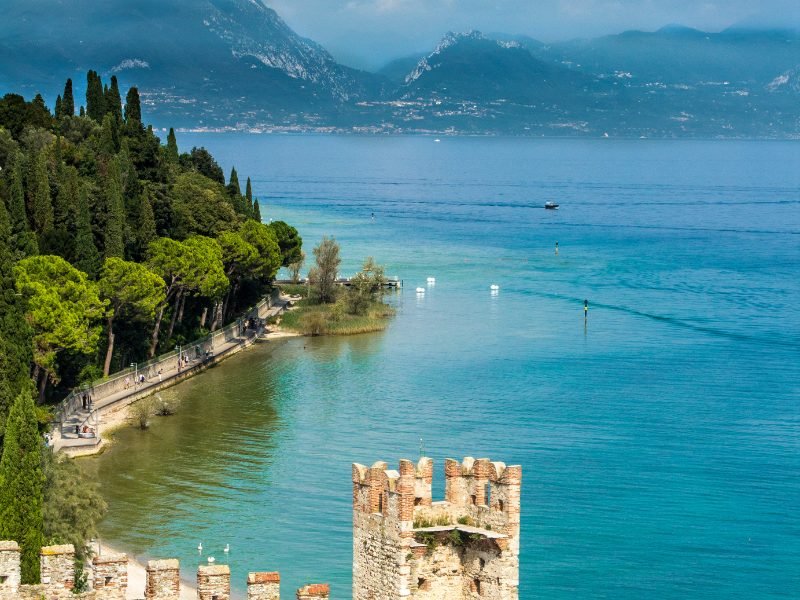 The town of Sirmione on Lake Garda with castle-like turrets overlooking the lake, trees, boats, etc.