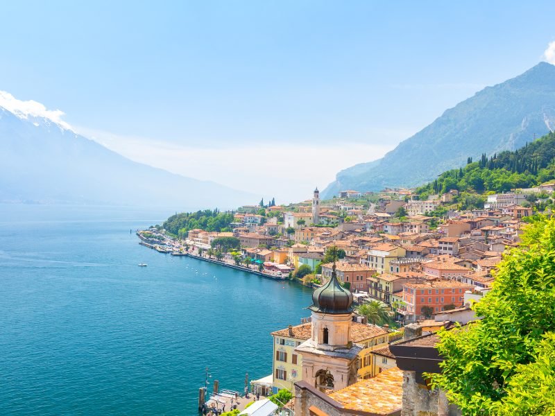 The town of Limone sul Garda with colorful buildings and mountains in background with harborfront walkway and boat approaching the town
