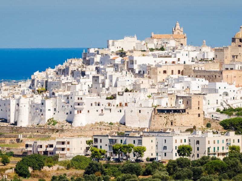 The hillside white city of Ostuni with church and white buildings and the azure sea in the background horizon