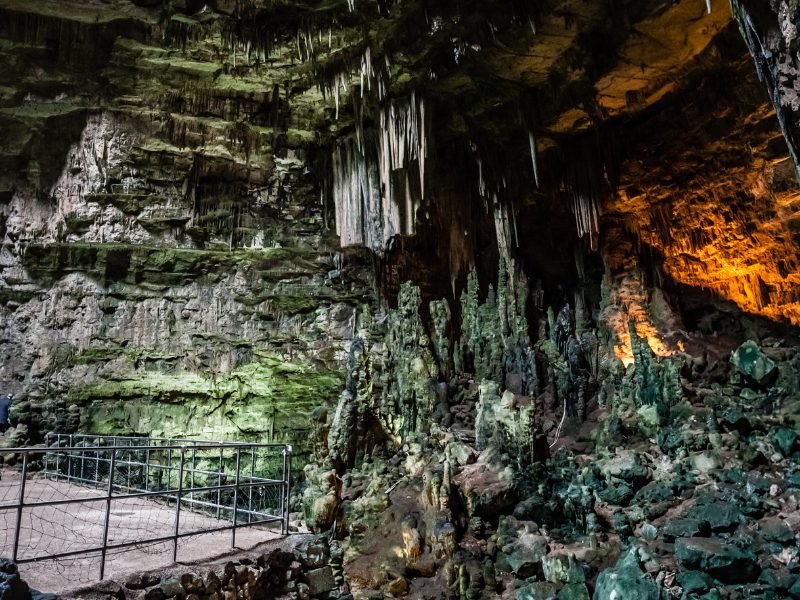 karst cave system with lighting and boardwalk with greenish tinted stalagmites and stalactites