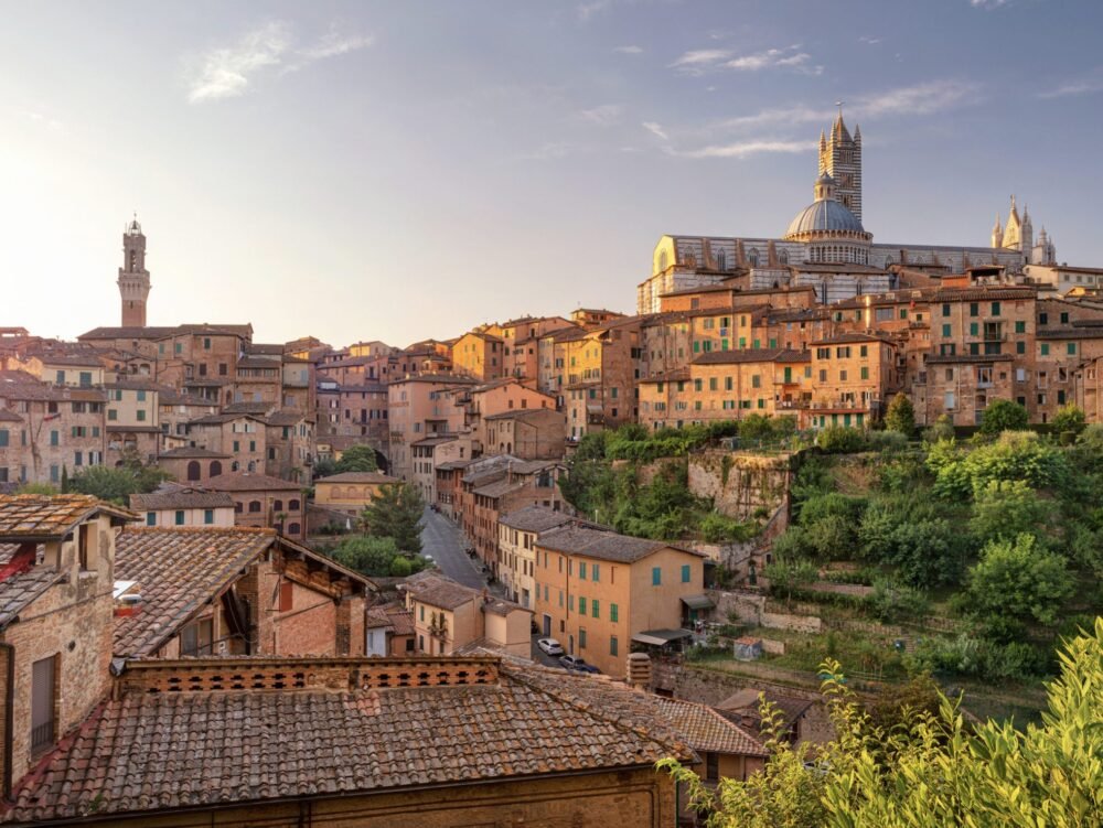 The city of Siena in Italy's Tuscany region at sunset with the cathedral and beautiful yellow-toned architecture around the city