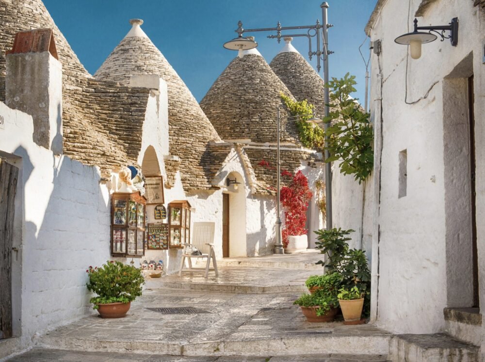 The trulli houses (conical white houses with stone roofs) on a cobblestone road in Puglia Italy, one of the must-stop places while on an Italy road trip of Puglia