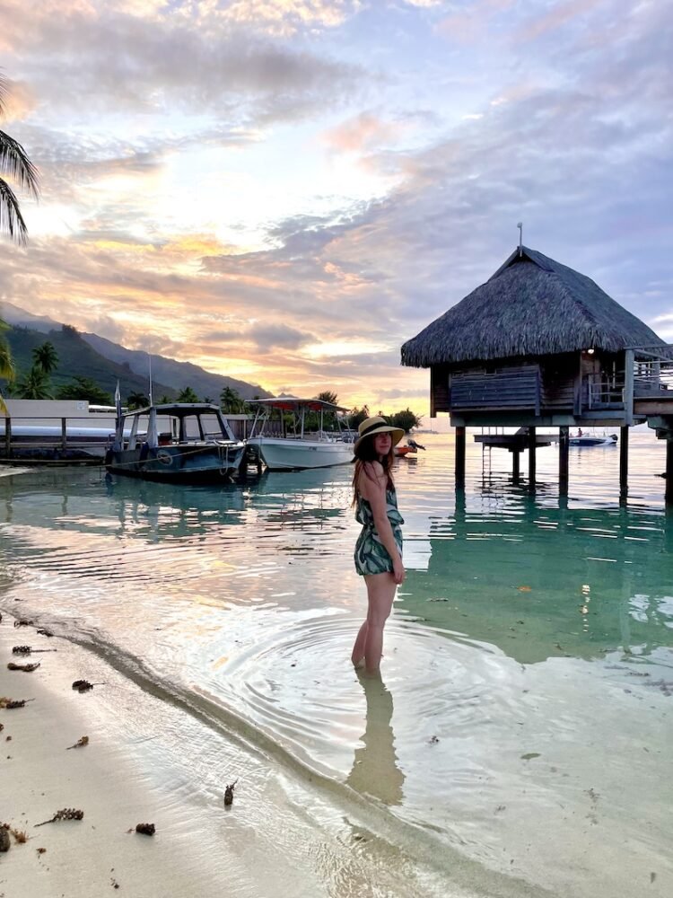 Allison in a sunhat and romper in front of the Manava bungalows at sunset