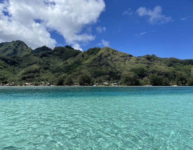The colorful turquoise waters of Moorea with the background of Moorea in the distance, as seen from a snorkeling boat in the lagoon