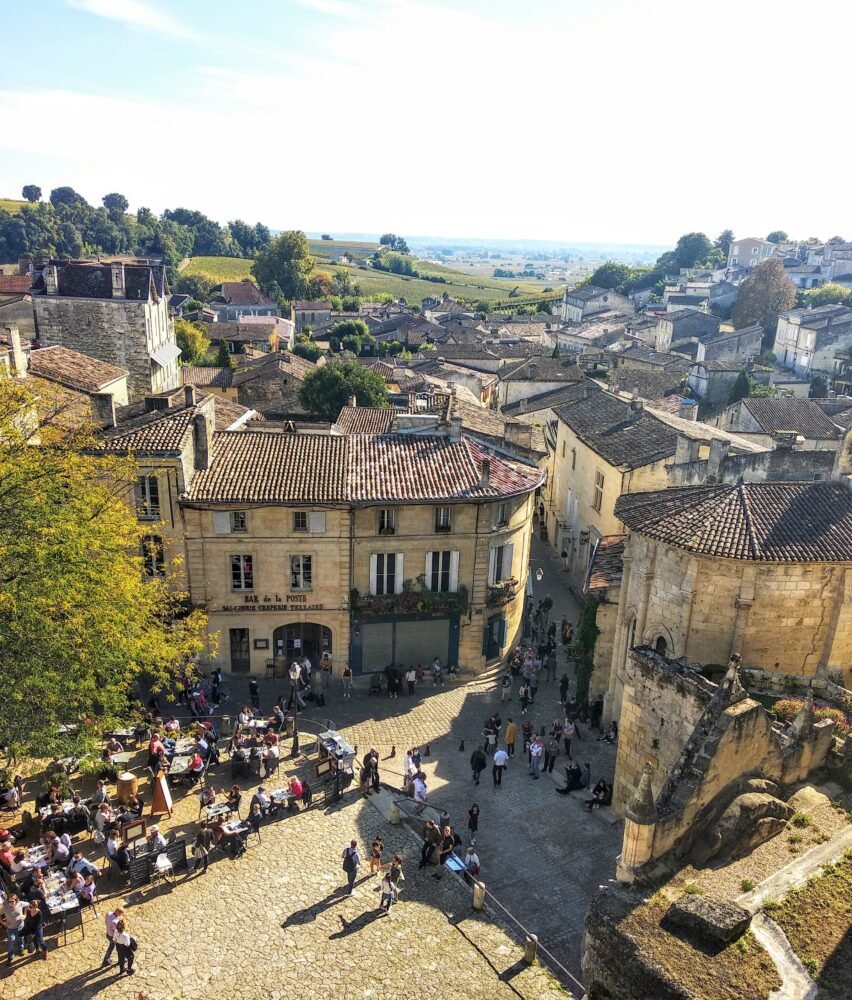 A view of the city streets of Saint Emilion, a charming medieval hilltop town with old architecture and lot sof people in the plaza, some sitting and dining